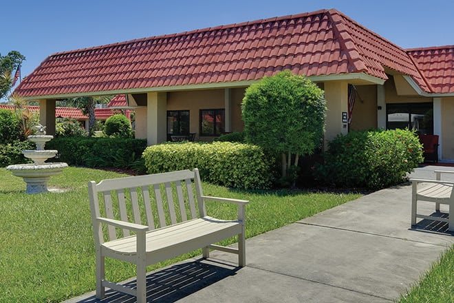 A quiet outdoor scene with a bench beside a sidewalk in front of a building with a red-tiled roof.