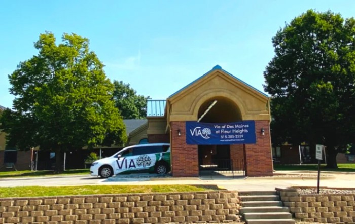 A vehicle parked in front of a community center with a banner displaying 'VIA' and promotional text.