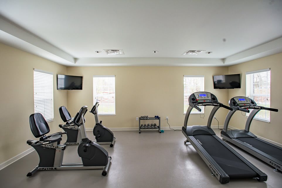 A small gym room featuring exercise bikes, a treadmill, and TV screens.