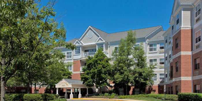 A multi-story residential building surrounded by trees under a clear blue sky.