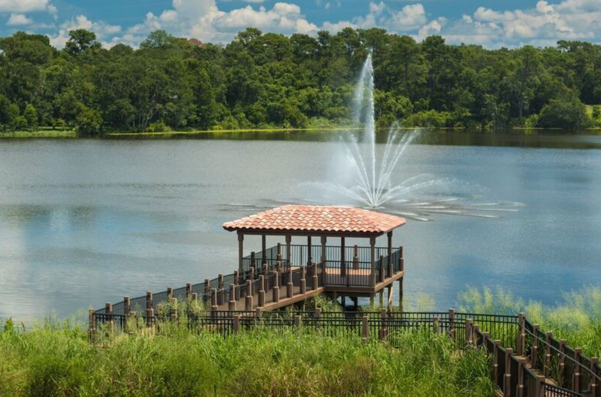 A scenic view of a lakeside gazebo with a fountain, surrounded by lush greenery.