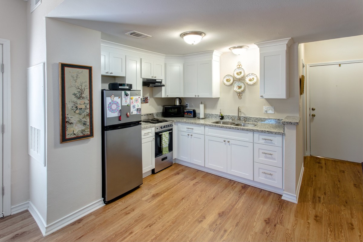 A modern kitchen with white cabinets, stainless steel appliances, and wood flooring.