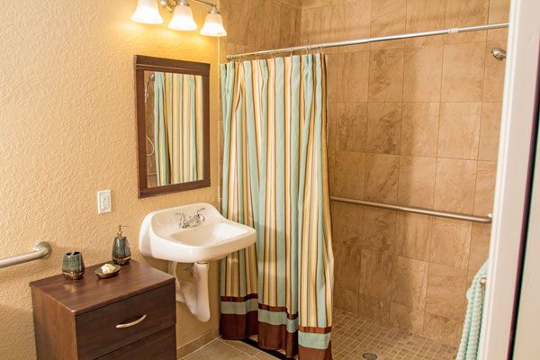 A cozy bathroom featuring a striped shower curtain, wall-mounted sink, and mirror with warm lighting.