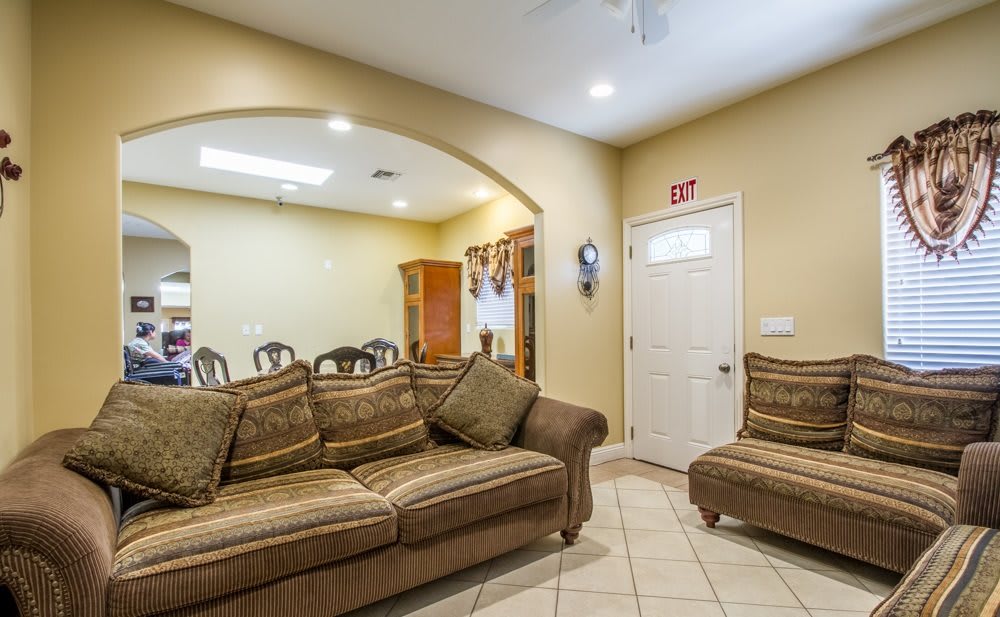 A cozy living room with a couch and armchair, adjacent to a dining area through an archway.