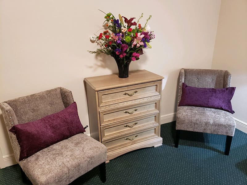 A cozy living room setup with two chairs, a wooden cabinet, and a vibrant floral arrangement.
