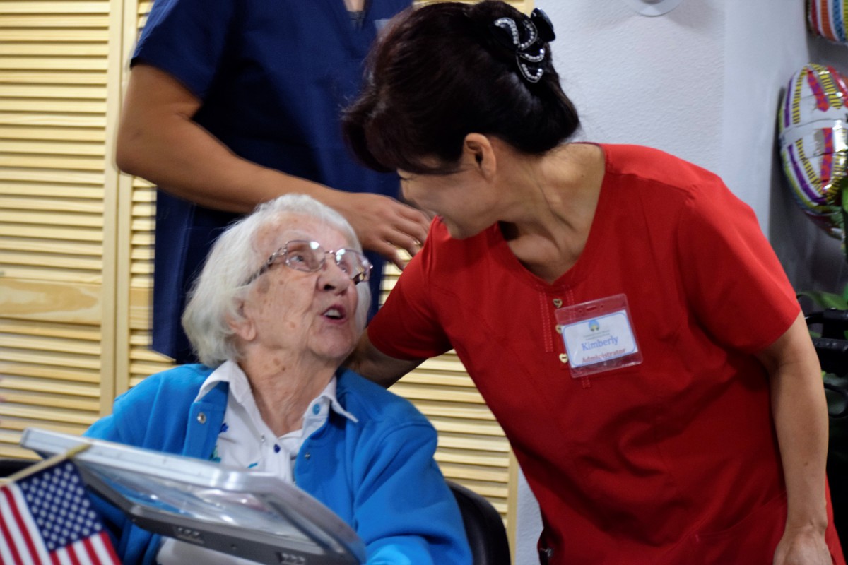 A nurse interacts with an elderly woman in a wheelchair, providing care and support.