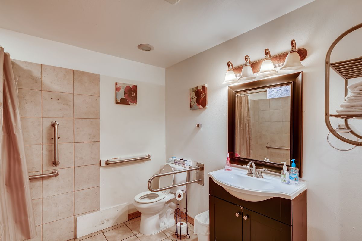 A modern bathroom with a sink, mirror, and toilet, featuring tiled flooring and a well-lit interior.
