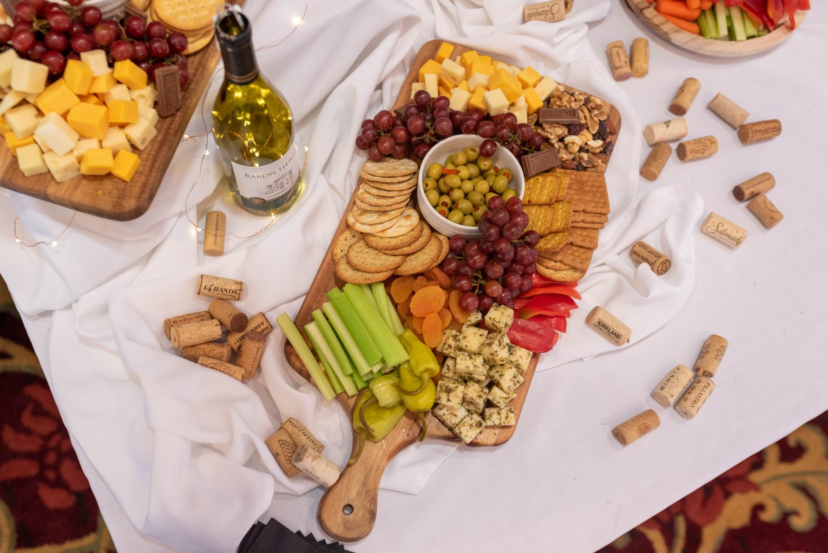 A beautifully arranged cheese and charcuterie board with an assortment of snacks, accompanied by a bottle of wine.