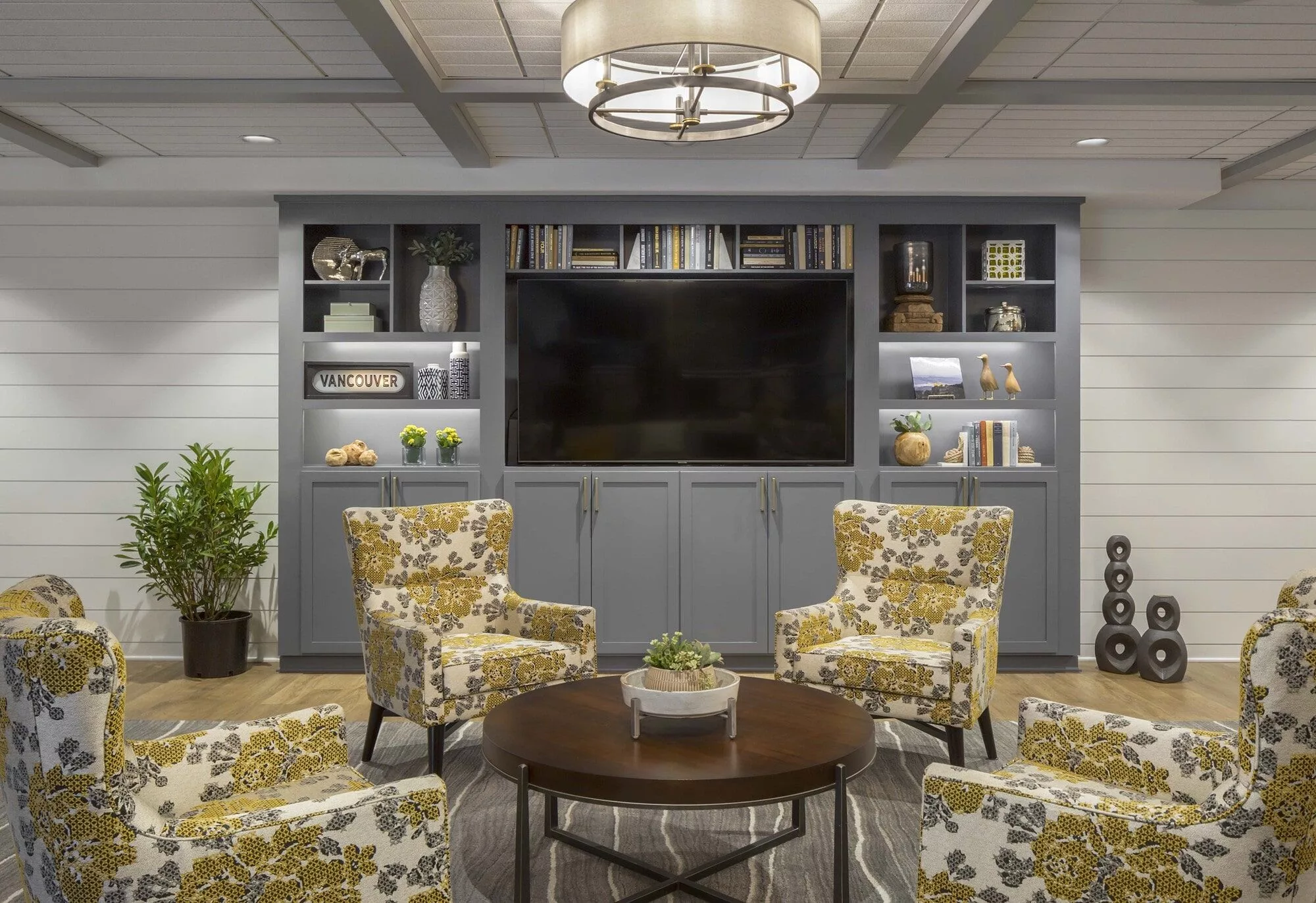 A cozy living room with floral chairs and a large television, surrounded by shelves filled with decor.