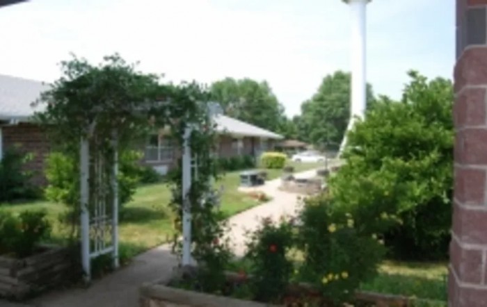 A serene garden with a pathway, lush greenery, and an archway leading to a building.