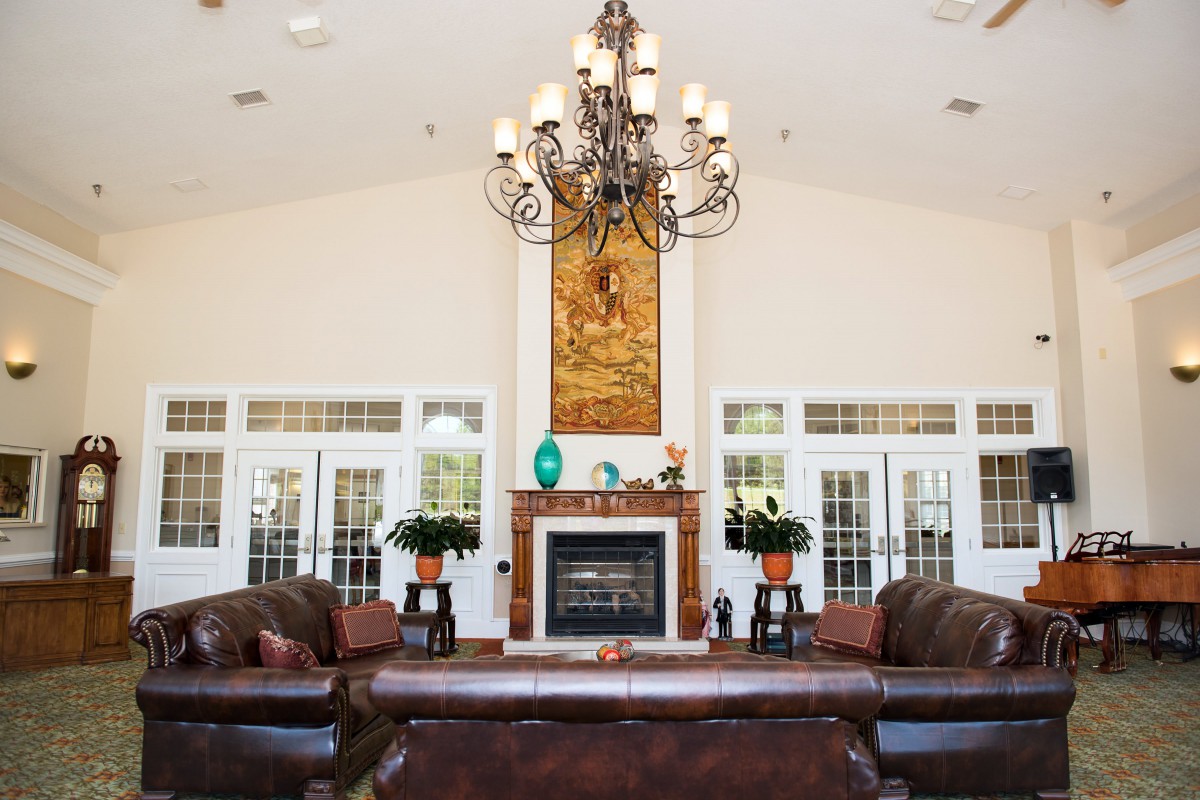 A spacious living room featuring a central fireplace, elegant chandelier, and leather sofas.