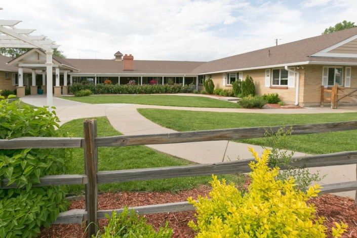 A building with a landscaped garden, featuring a wooden fence, pathway, and green lawn under a partly cloudy sky.