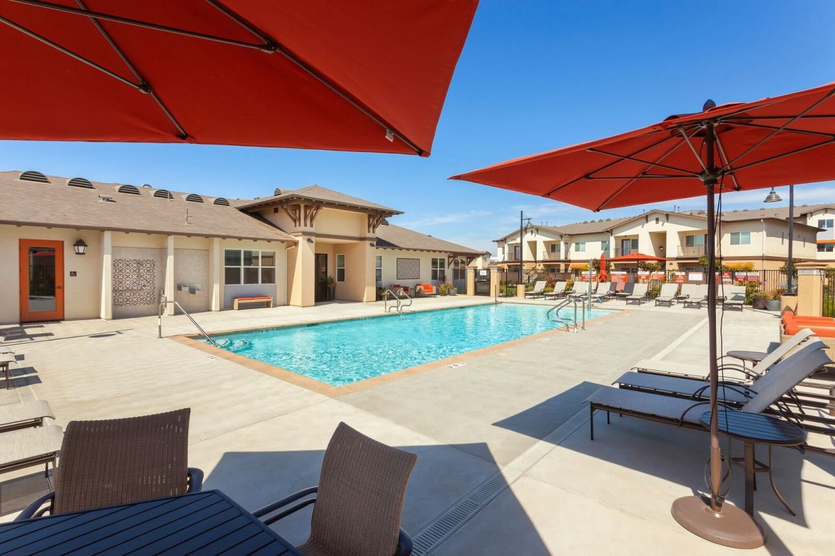 A sunny day by the pool in a residential area with lounge chairs and umbrellas.