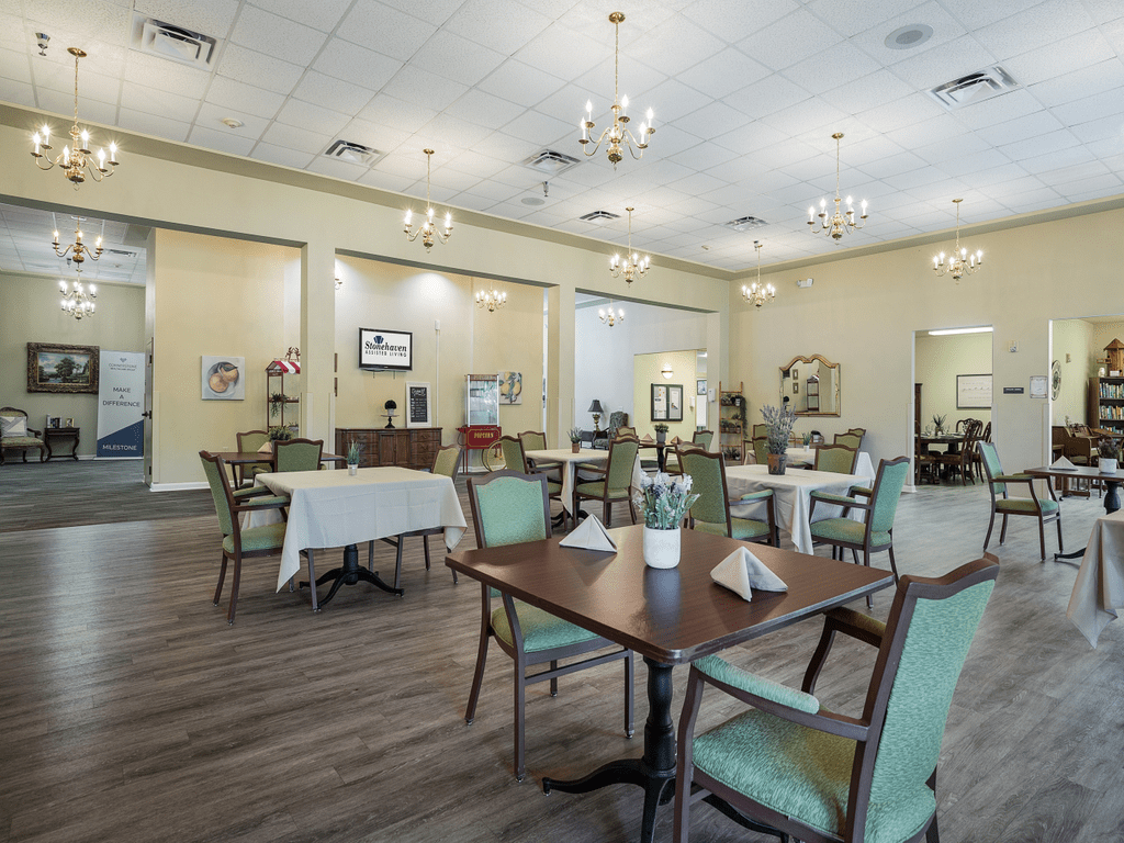 A spacious and elegantly furnished dining area with tables and chairs, featuring chandeliers and bright lighting.