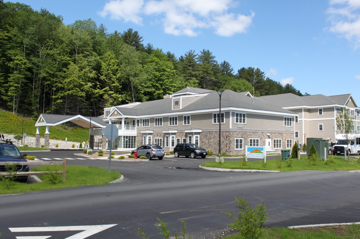 A modern office building with a parking lot and surrounding greenery under a clear blue sky.