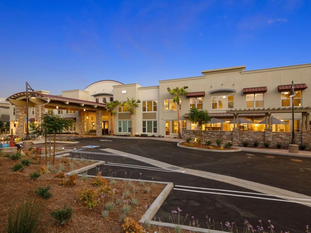 A modern residential building with a well-lit exterior in the evening, featuring a spacious parking area.