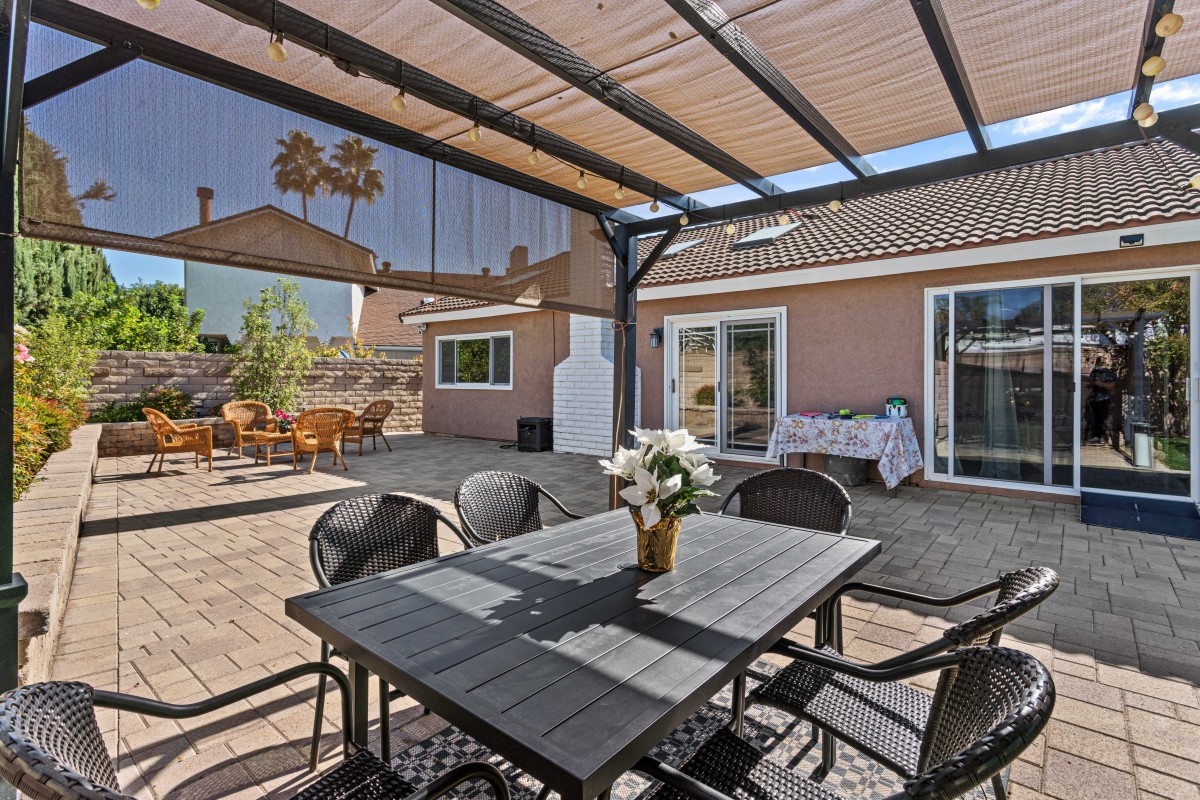 A sunny backyard patio with a pergola, featuring a dining table and chairs.