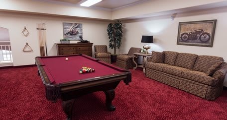 A cozy game room featuring a pool table with red felt, surrounded by comfortable seating and stylish decor.
