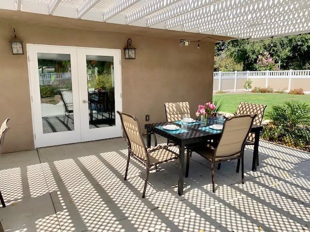 A cozy patio dining area with a table set for four under a pergola casting patterned shadows.