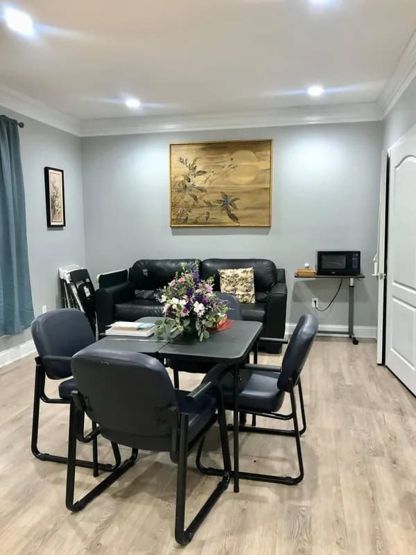 A cozy living room with a dining area featuring a table, chairs, sofa, and decorative elements like flowers and paintings.