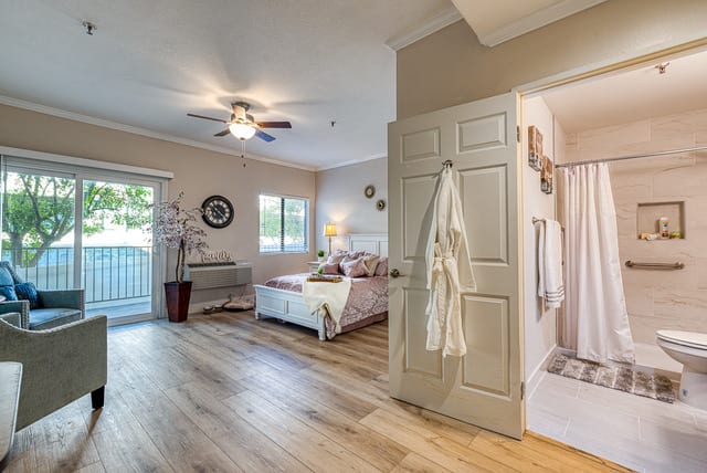A modern bedroom with wood flooring, natural light, and an adjoining bathroom.