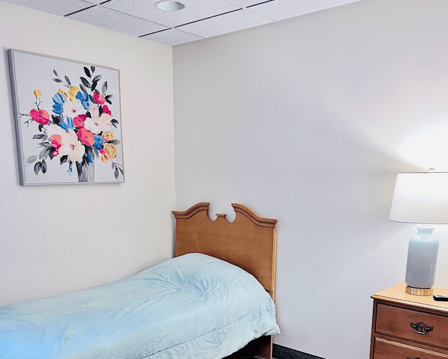 A minimalist bedroom with a single bed, wall art, and a lamp.
