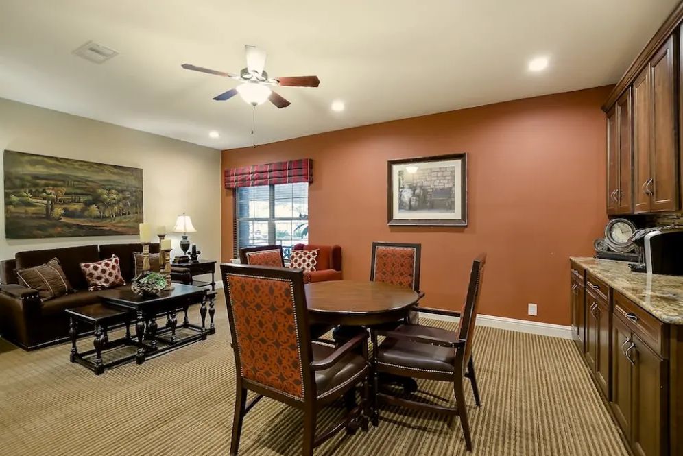 A cozy living room with a dining area, featuring a round table and chairs, a ceiling fan, and warm earth-tone walls.