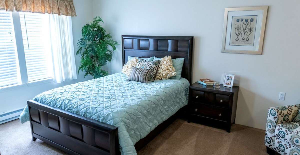 A cozy bedroom with a neatly made bed, decorative pillows, and a nightstand beside it.