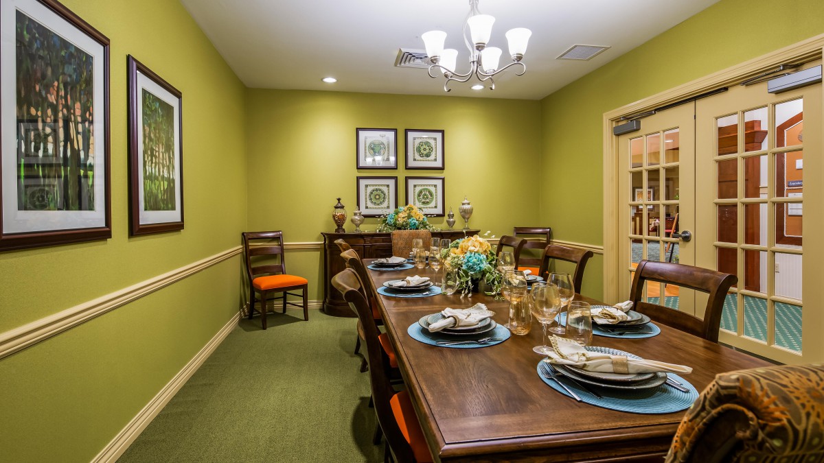 A well-decorated dining room with a large wooden table, elegant place settings, and decorative artwork on green walls.