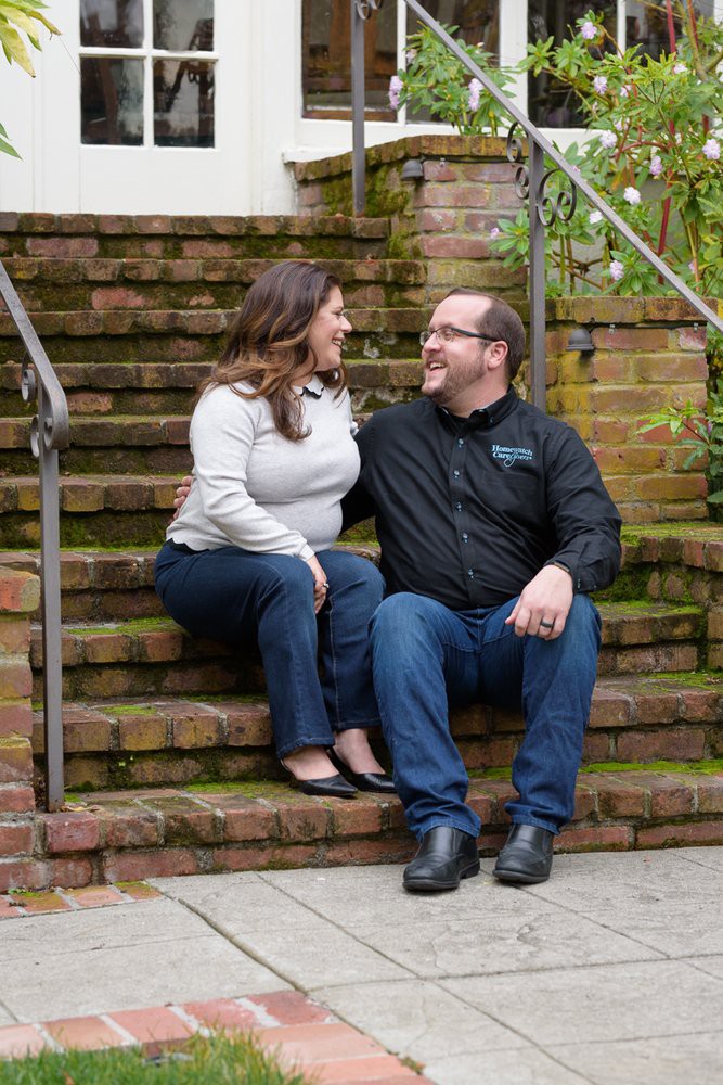 A couple sitting on outdoor brick stairs, smiling at each other.
