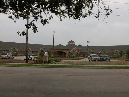 A view of a healthcare facility from the street, featuring a landscaped entrance and parked vehicles.