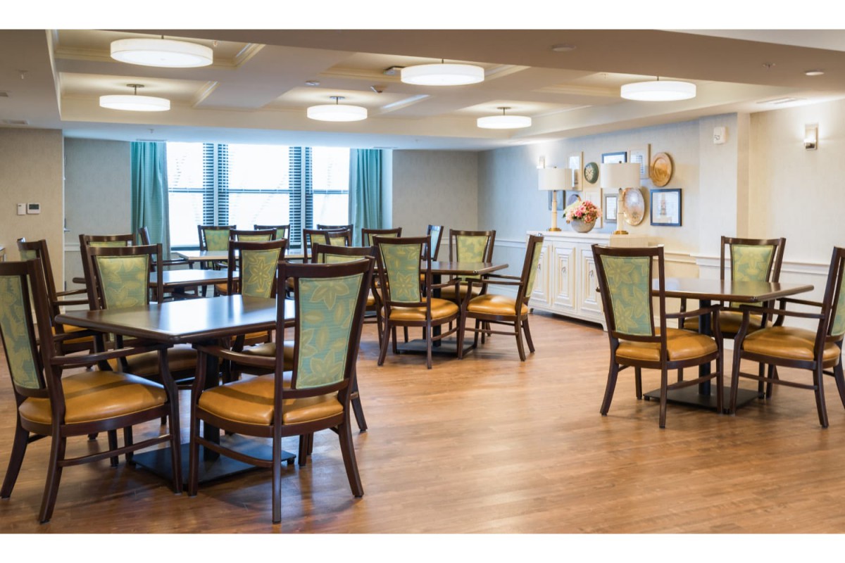 A spacious dining room featuring multiple tables and chairs, with wood flooring and decorative wall art.