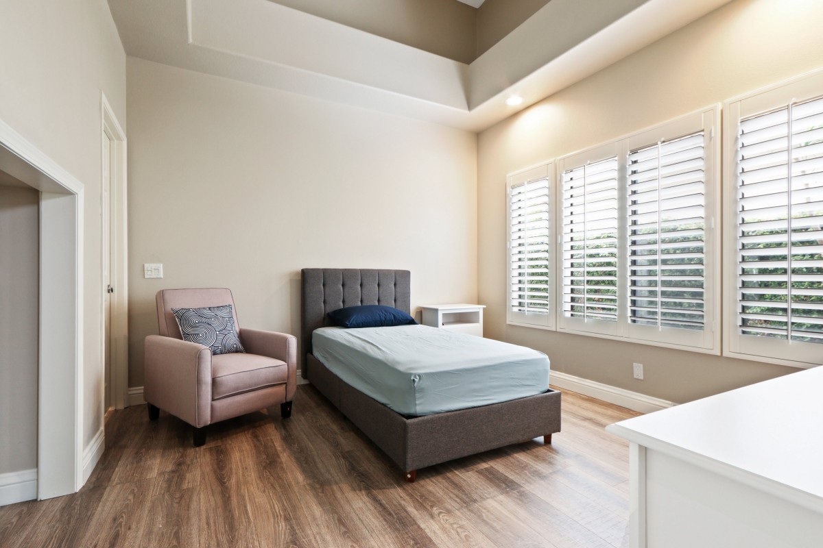 A minimalist bedroom with a single bed and an armchair by the window.