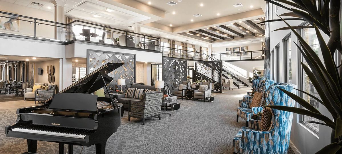 A spacious and elegant lounge area featuring a grand piano, modern furniture, and a stylish staircase.