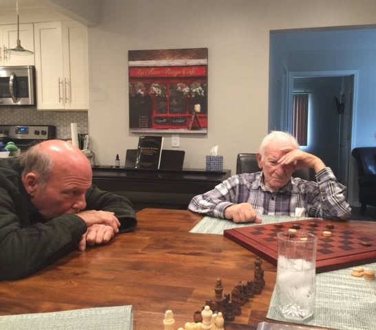 Two elderly men sitting at a table playing a board game.