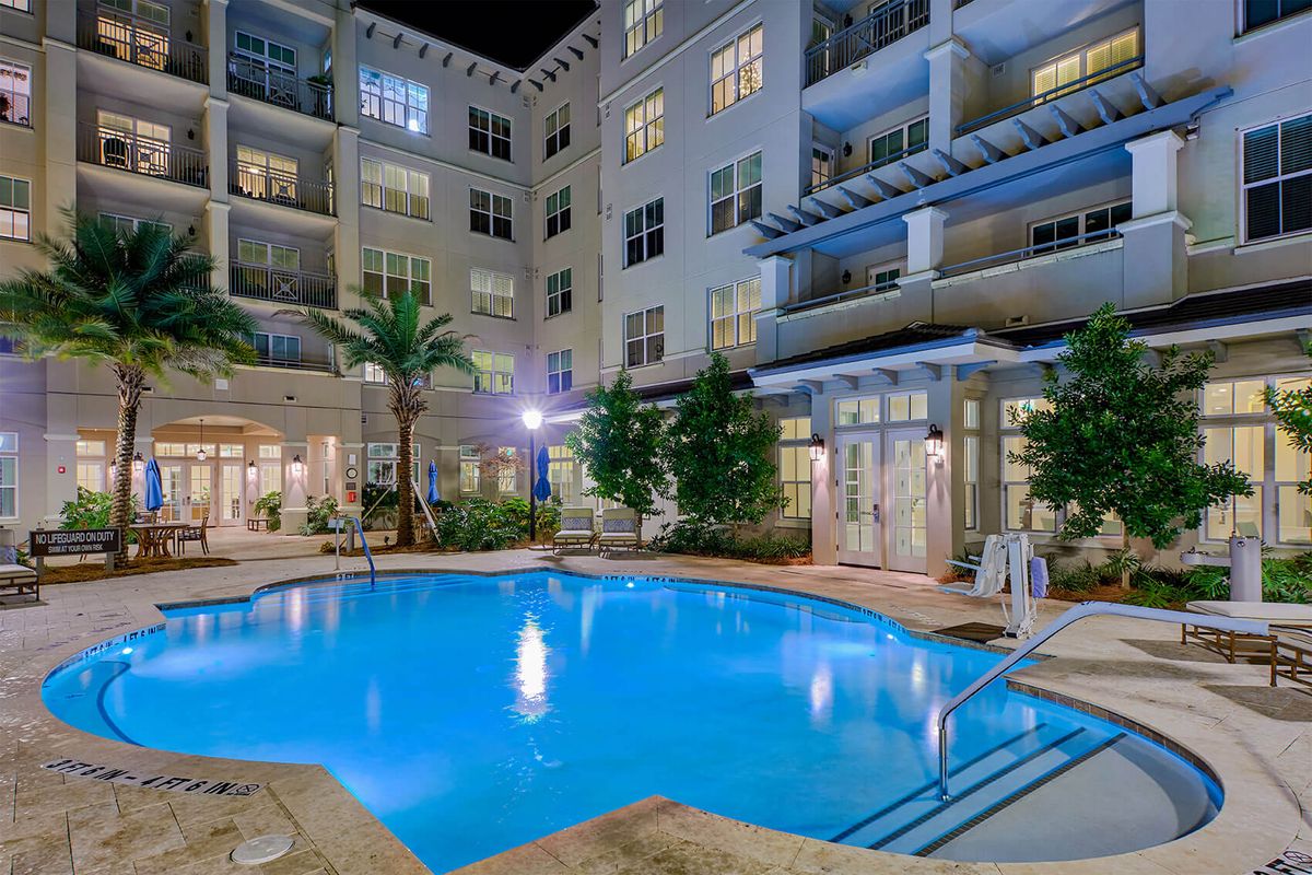 A modern apartment complex with a well-lit swimming pool area at night.
