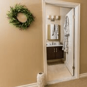 A view into a bathroom through an open doorway, featuring a mirror above the sink and a wreath on the wall.