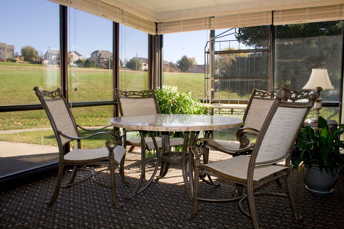 A cozy screened-in porch with a glass table and chairs overlooking a garden.