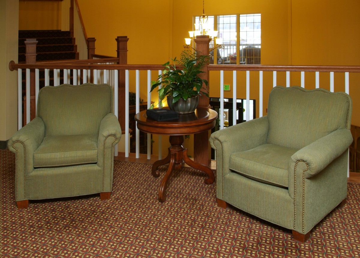 A cozy living room setup featuring two green armchairs and a wooden table with a plant, set against a warm yellow background.