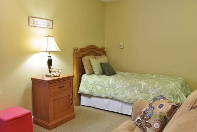 A cozy bedroom with a single bed and a nightstand featuring a lamp.