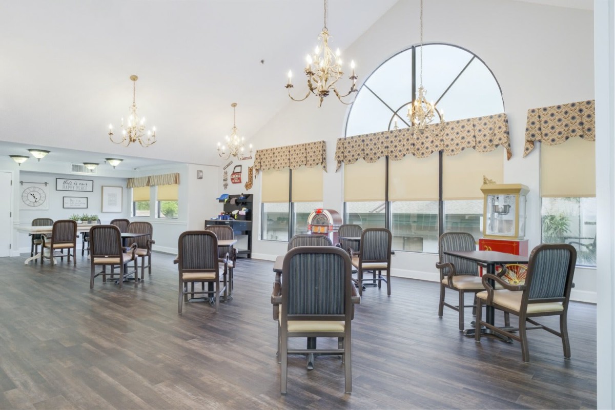 A spacious and bright dining area featuring chandeliers, tables with chairs, and large windows.