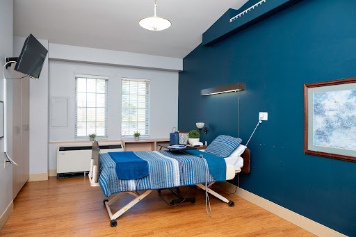 A modern hospital patient room featuring a blue accent wall, minimal furnishings, and natural light.