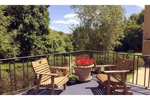 A peaceful patio setting with wooden chairs and a flower pot, surrounded by lush greenery.