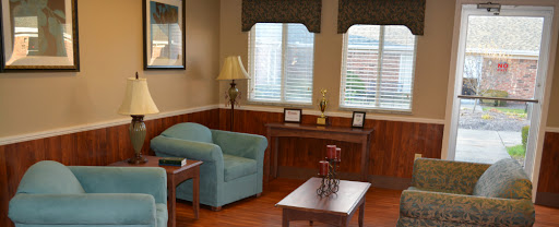 A cozy living room with a soft blue sofa, a wooden table, and natural light streaming through the windows.
