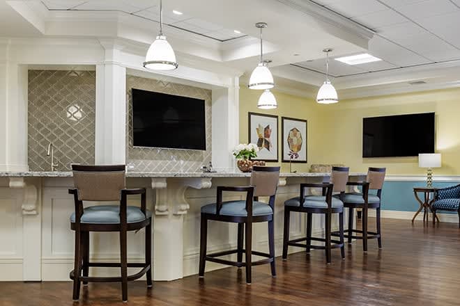A modern bar area with high chairs, pendant lighting, and a large television.