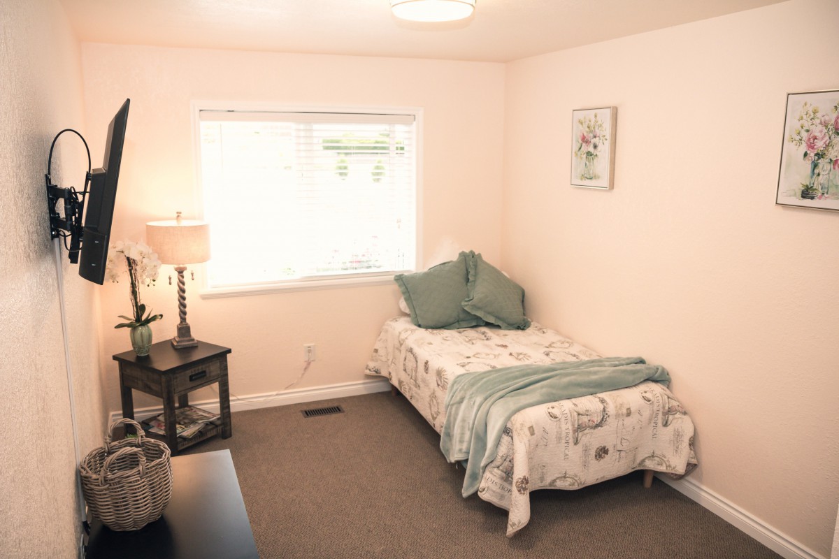 A minimalist bedroom featuring a single bed, a lamp, and a window providing natural light.