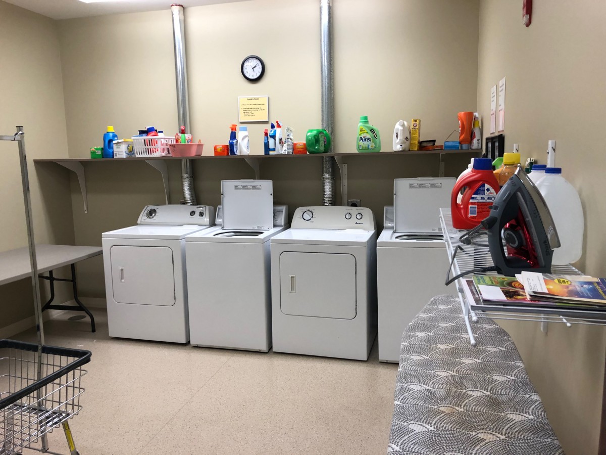 A laundry room with washing machines, dryers, and shelves stocked with detergent bottles.