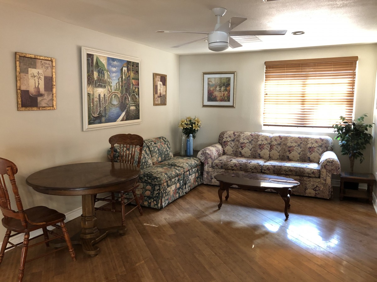 A cozy living room with a floral sofa, wooden table set, and wall art.