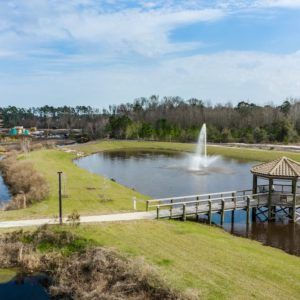 A scenic view of a pond with a fountain and gazebo surrounded by lush greenery and pathways.