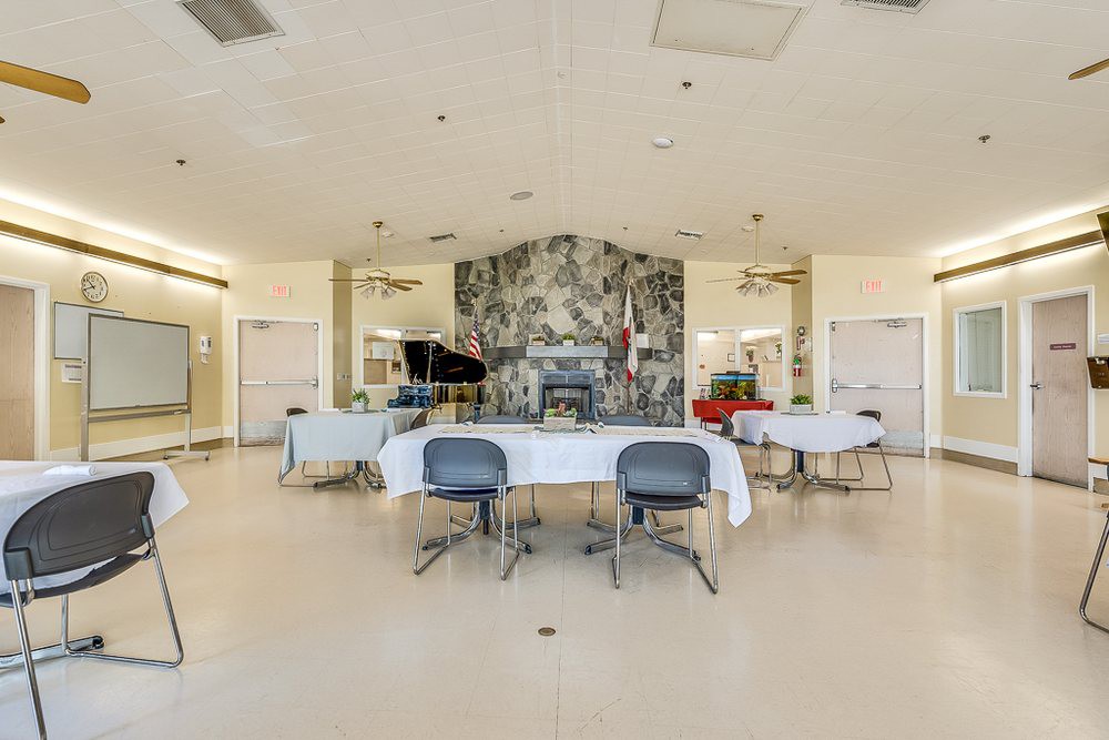 A spacious event room featuring a piano and tables set with chairs, highlighted by a decorative wall mural.